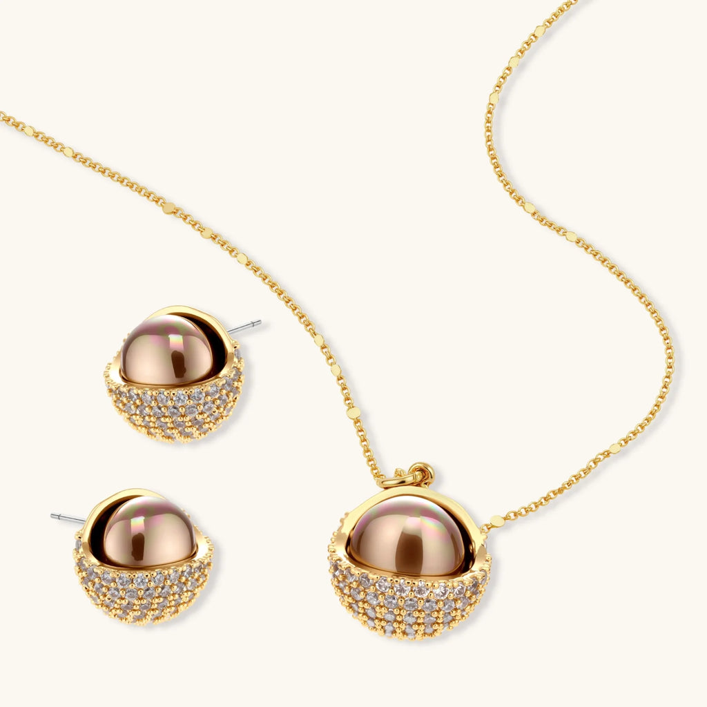 Elegant spherical pendant necklace and earrings set featuring crystal-pavé bottom half in gold or silver finish on white background.