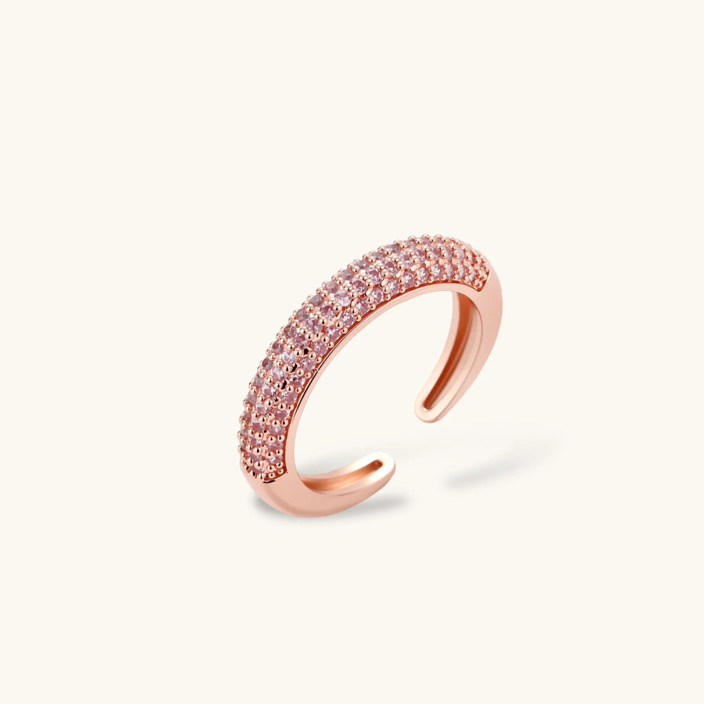 Rose gold jewelry set with pavé cubic zirconia stones including curved necklace, hoop earrings, and adjustable ring on cream background.
