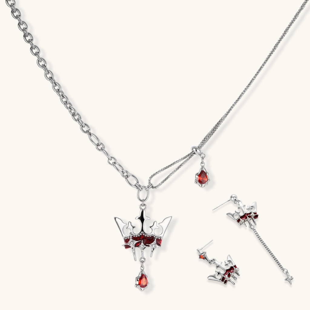 Silver-tone crown pendant with red zirconia stones and matching asymmetrical earrings on cream background