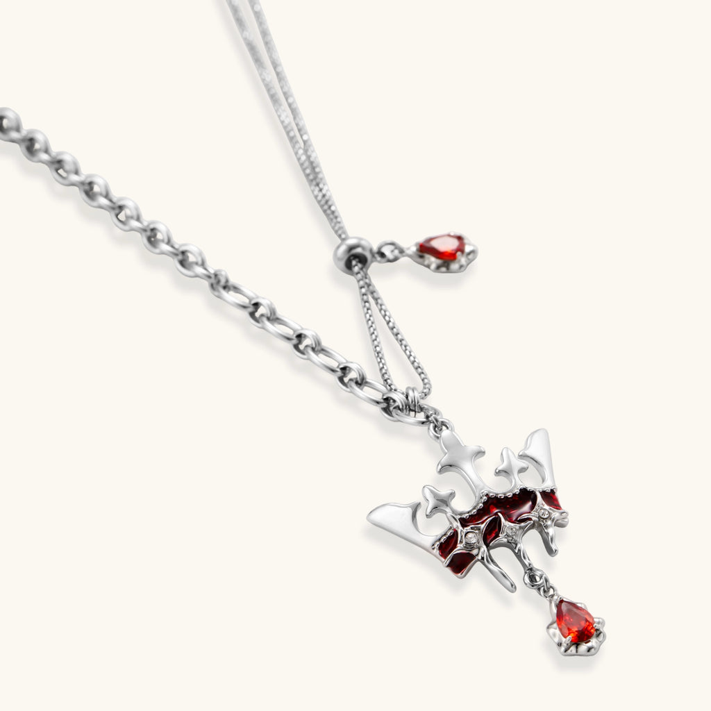 Silver-tone crown pendant with red zirconia stones and matching asymmetrical earrings on cream background