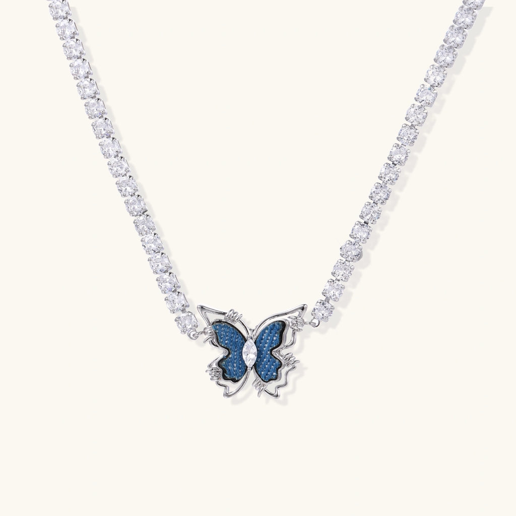 White gold plated tennis necklace with blue denim butterfly pendant and clear zirconia stones on cream background