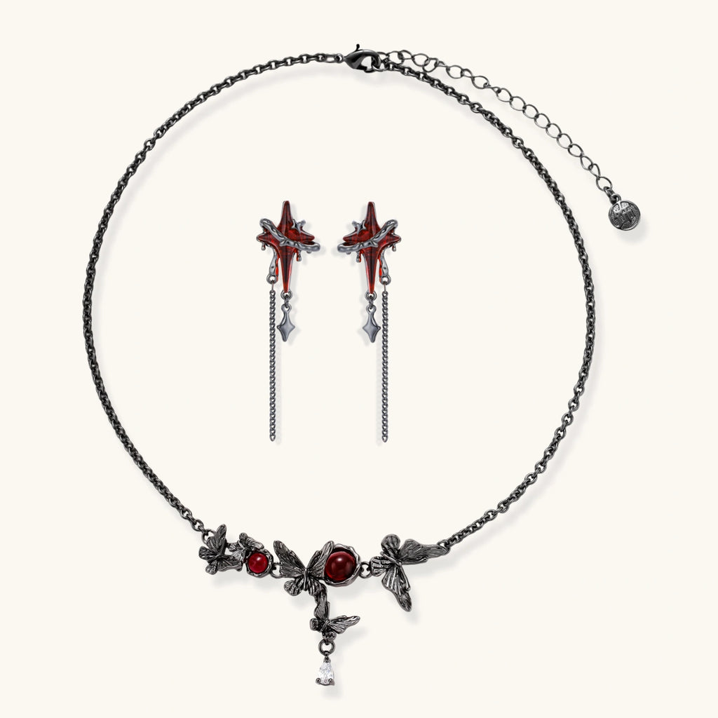 Gothic jewelry set with red resin cross pendants wrapped in dark metal chains on cream background.