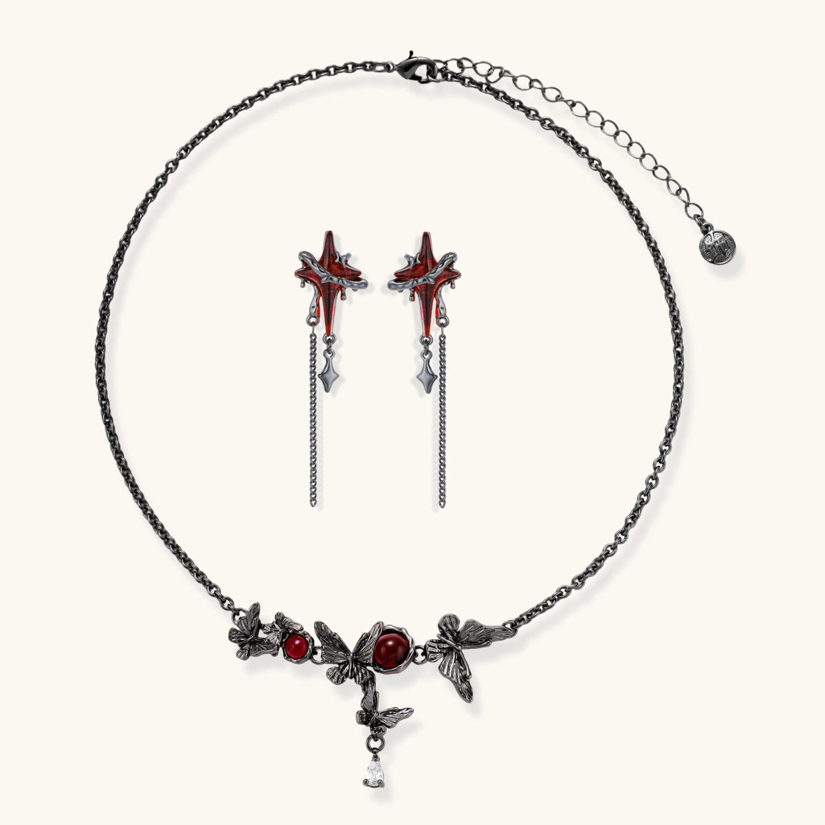 Gothic jewelry set with red resin cross pendants wrapped in dark metal chains on cream background.