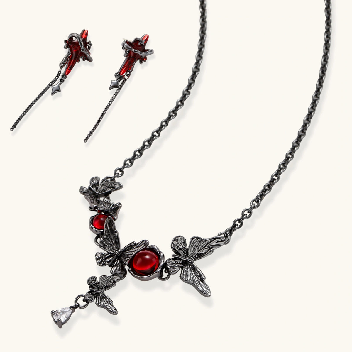Gothic jewelry set with red resin cross pendants wrapped in dark metal chains on cream background.