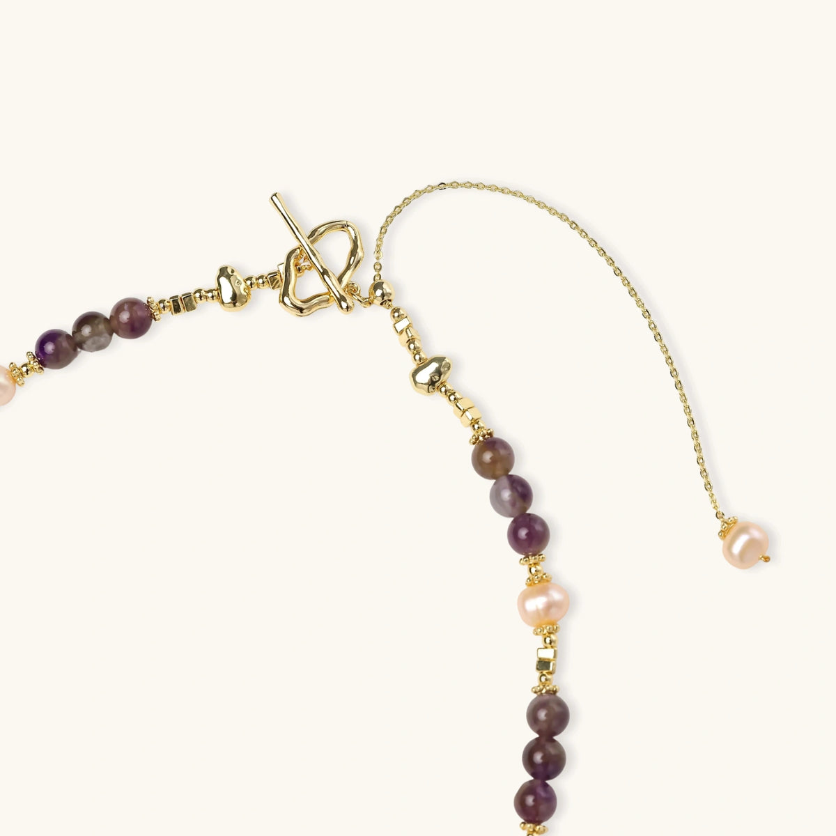 Gold necklace with iridescent baroque pearl pendant, purple amethyst beads, and crystal star charm on cream background